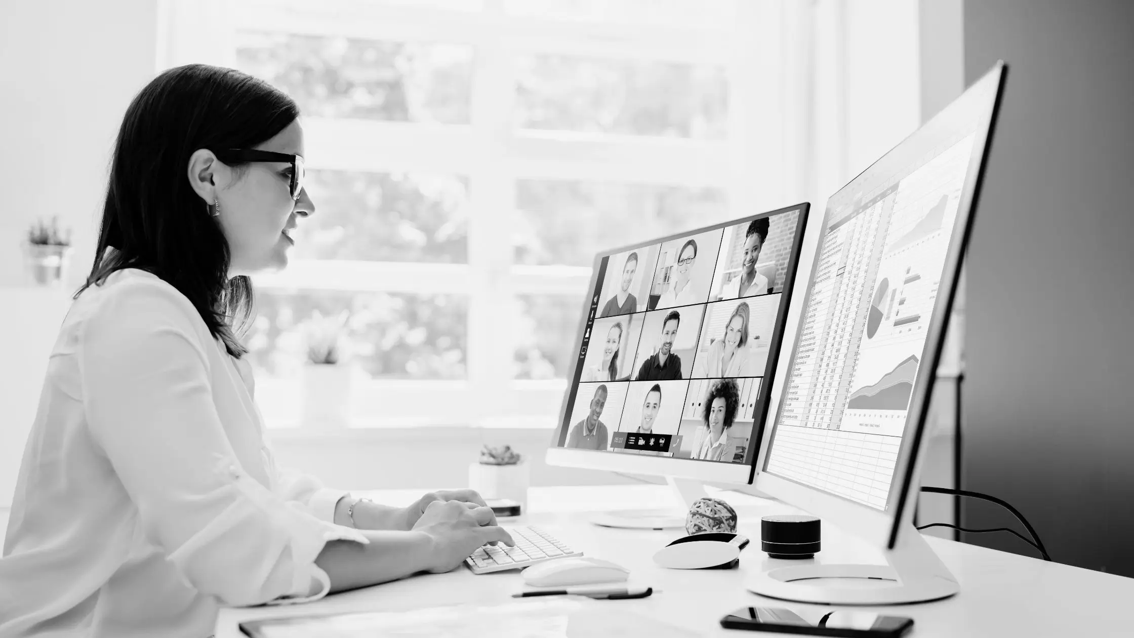 A woman sits at a desk, focused on multiple computer monitors displaying and online meetings and data.
