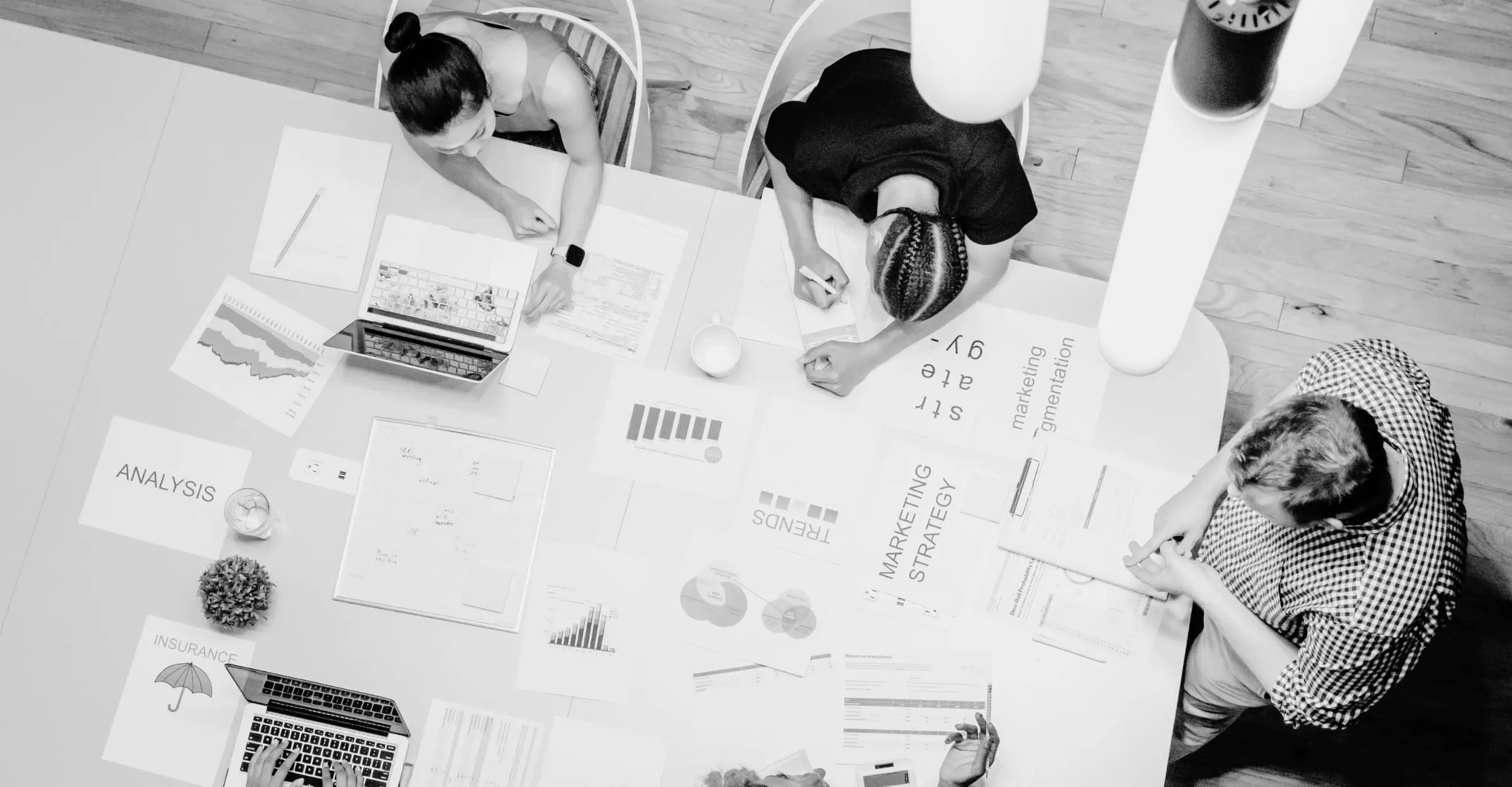 Aerial perspective of a group of people engaged in teamwork, working on documents and digital devices at a shared workspace.